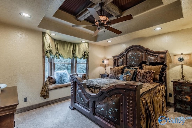 bedroom with a raised ceiling, light carpet, a textured wall, and baseboards