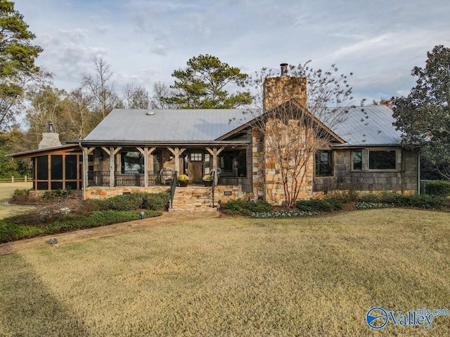 view of front of property featuring a sunroom, a chimney, metal roof, and a front yard