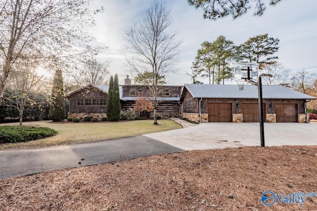 view of front of property featuring metal roof, stone siding, a front lawn, and driveway