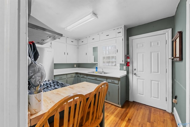 kitchen featuring stainless steel refrigerator, gray cabinetry, sink, light hardwood / wood-style flooring, and ventilation hood