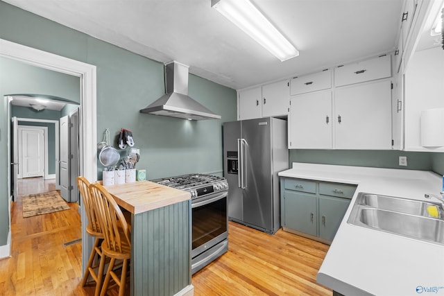 kitchen with light wood-type flooring, stainless steel appliances, sink, wall chimney range hood, and white cabinetry