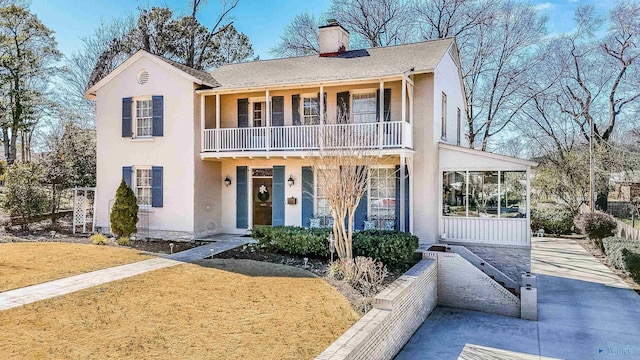 view of front of property featuring a balcony, a chimney, a front lawn, and stucco siding