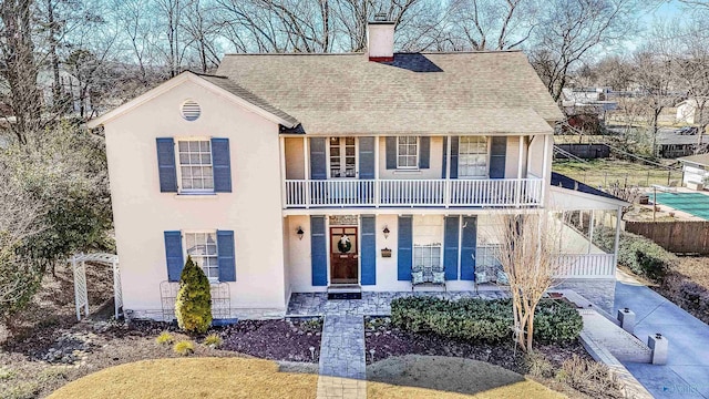 view of front of home with a balcony, a chimney, roof with shingles, fence, and a porch