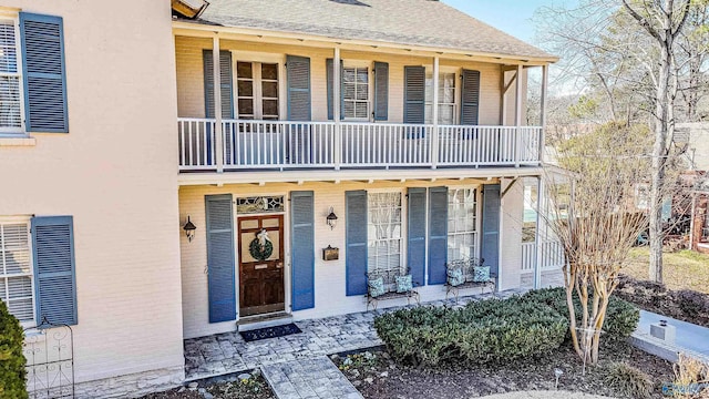 view of front of property featuring a shingled roof, brick siding, and a balcony