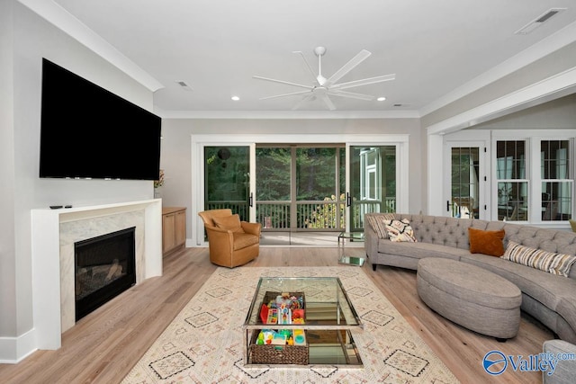 living room featuring light hardwood / wood-style floors, a high end fireplace, ceiling fan, french doors, and ornamental molding