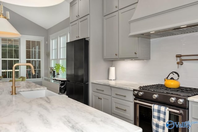 kitchen featuring decorative backsplash, stainless steel range with gas cooktop, premium range hood, sink, and black fridge