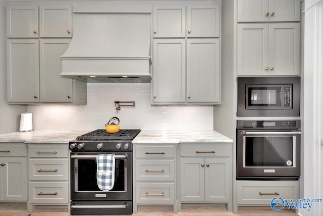 kitchen featuring decorative backsplash, stainless steel appliances, light stone counters, and custom range hood