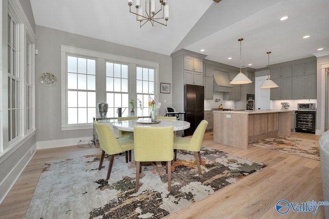 dining space featuring light hardwood / wood-style flooring, beverage cooler, vaulted ceiling, and a notable chandelier