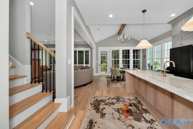 kitchen featuring light stone countertops, light wood-type flooring, vaulted ceiling with beams, and a wealth of natural light