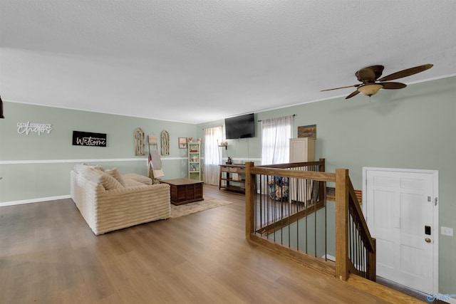 living room with a textured ceiling, ceiling fan, and wood finished floors