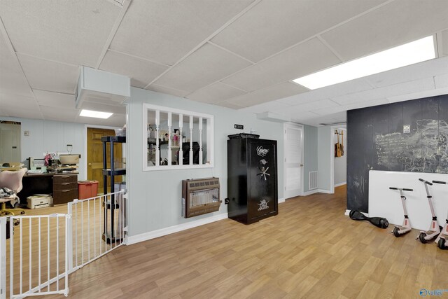 below grade area featuring a paneled ceiling, light wood-type flooring, visible vents, and heating unit