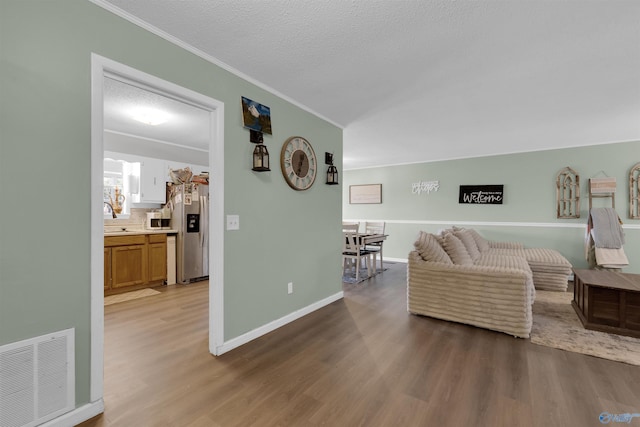 living area with light wood-type flooring, a textured ceiling, visible vents, and crown molding