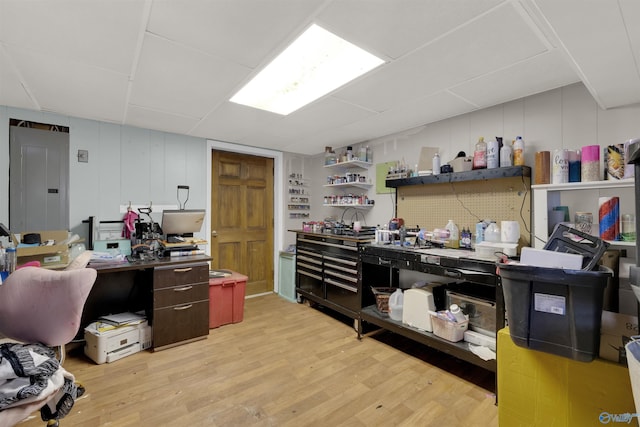 home office featuring electric panel, a decorative wall, light wood-style flooring, and a workshop area