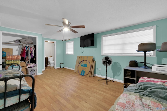 bedroom with baseboards, connected bathroom, ceiling fan, wood finished floors, and a closet