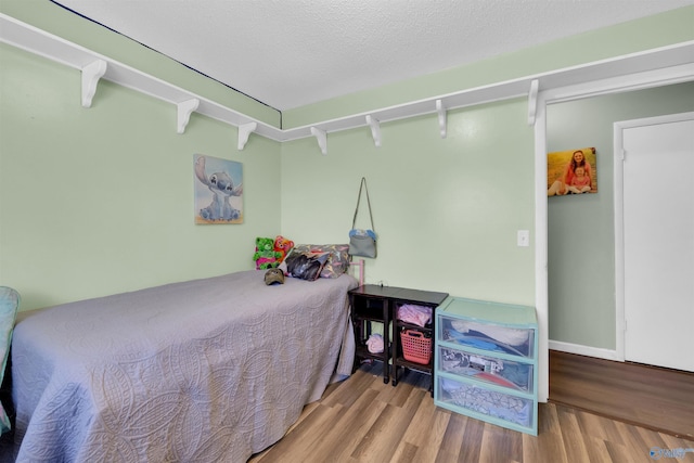 bedroom with a textured ceiling, baseboards, and wood finished floors