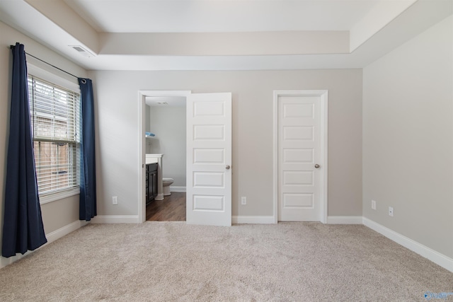 unfurnished bedroom with visible vents, baseboards, a raised ceiling, ensuite bath, and carpet floors