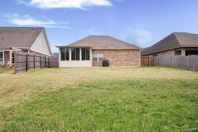 back of property with a fenced backyard, brick siding, a sunroom, and a yard