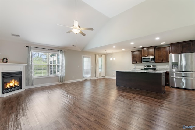 kitchen with dark brown cabinets, a ceiling fan, appliances with stainless steel finishes, open floor plan, and a glass covered fireplace