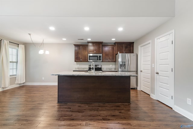 kitchen with stainless steel appliances, a center island with sink, dark brown cabinetry, dark wood-type flooring, and a sink