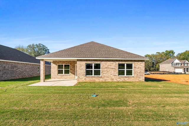 back of property featuring brick siding, roof with shingles, a lawn, and a patio