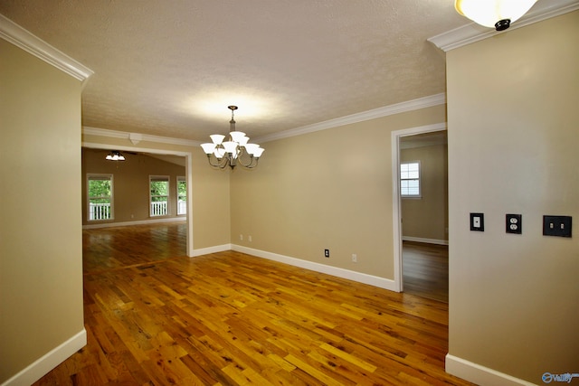 empty room with ornamental molding, wood-type flooring, a wealth of natural light, and a notable chandelier