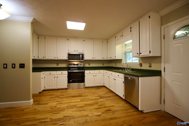 kitchen featuring appliances with stainless steel finishes, white cabinets, sink, light wood-type flooring, and ornamental molding