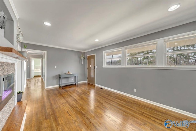 unfurnished living room featuring a tile fireplace, crown molding, baseboards, and wood finished floors