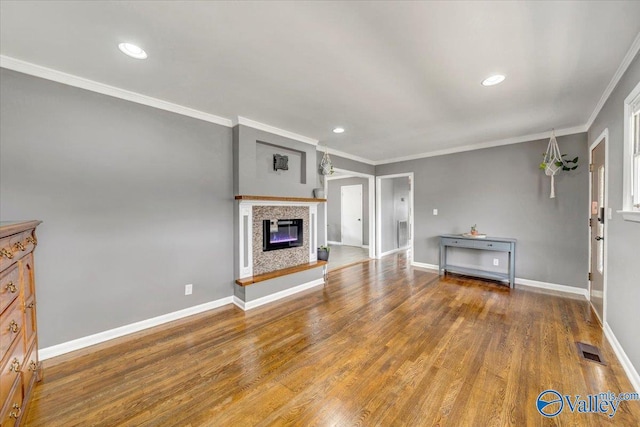 unfurnished living room featuring ornamental molding, a glass covered fireplace, baseboards, and wood finished floors