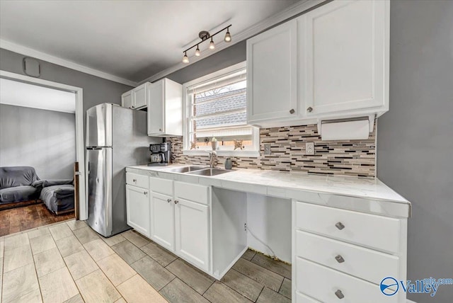 kitchen featuring tasteful backsplash, white cabinetry, a sink, and freestanding refrigerator