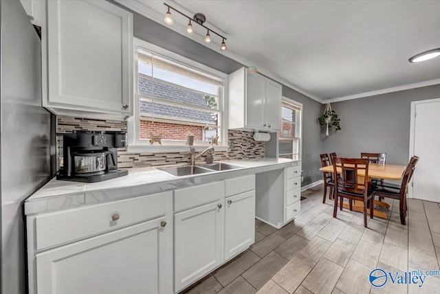 kitchen featuring freestanding refrigerator, a sink, crown molding, white cabinetry, and backsplash