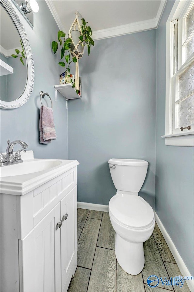 half bathroom featuring baseboards, toilet, crown molding, vanity, and wood finish floors