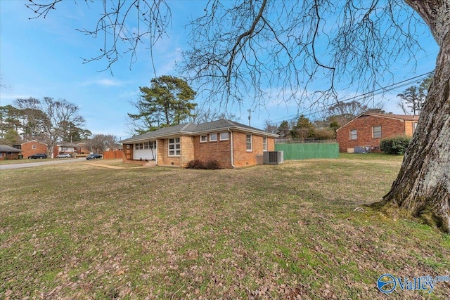 view of side of home featuring central AC unit, an attached garage, brick siding, crawl space, and a lawn