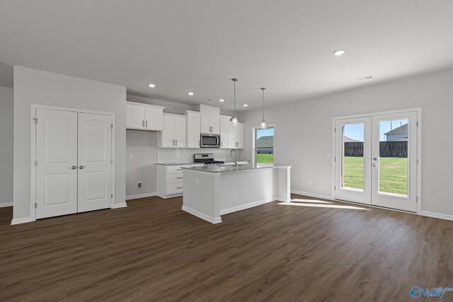 kitchen with appliances with stainless steel finishes, white cabinetry, an island with sink, pendant lighting, and dark wood-type flooring