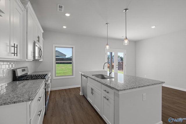 kitchen with white cabinets, stainless steel appliances, an island with sink, light stone counters, and sink