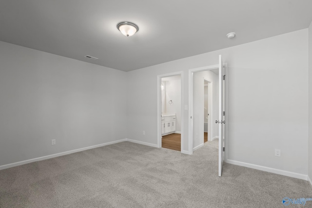 unfurnished bedroom featuring connected bathroom and light carpet