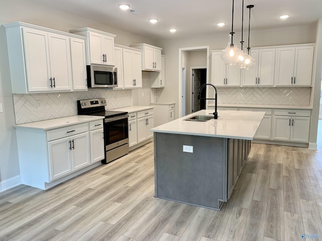 kitchen with light wood finished floors, a sink, stainless steel appliances, tasteful backsplash, and white cabinetry