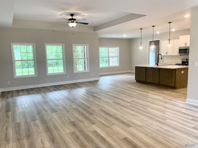 unfurnished living room featuring baseboards, a ceiling fan, light wood-style floors, and a sink