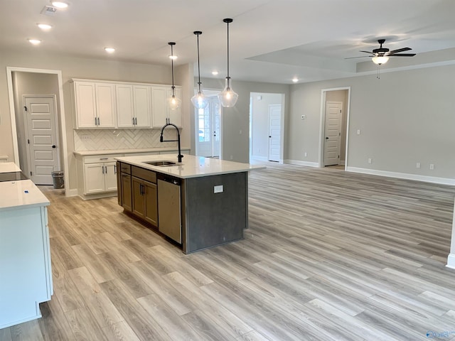 kitchen featuring tasteful backsplash, a sink, light countertops, dishwasher, and light wood finished floors