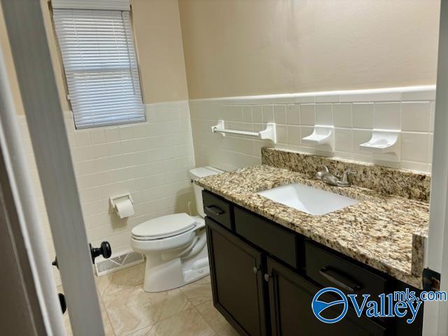 bathroom featuring toilet, vanity, visible vents, tile walls, and wainscoting