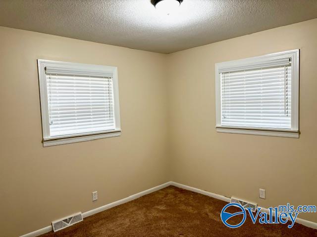 empty room featuring a textured ceiling, dark carpet, visible vents, and baseboards