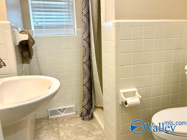 full bathroom featuring visible vents, toilet, tile patterned floors, curtained shower, and tile walls