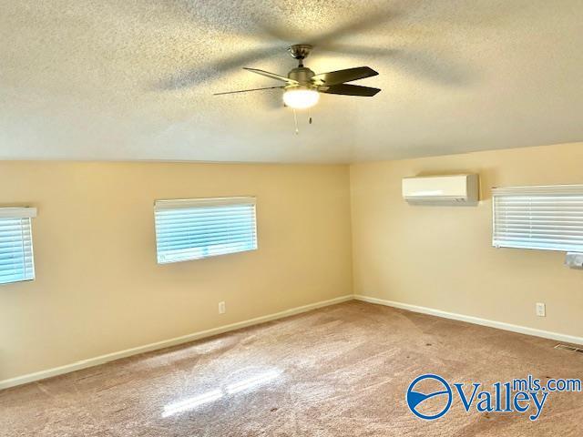 carpeted empty room with a healthy amount of sunlight, a wall mounted air conditioner, ceiling fan, and visible vents