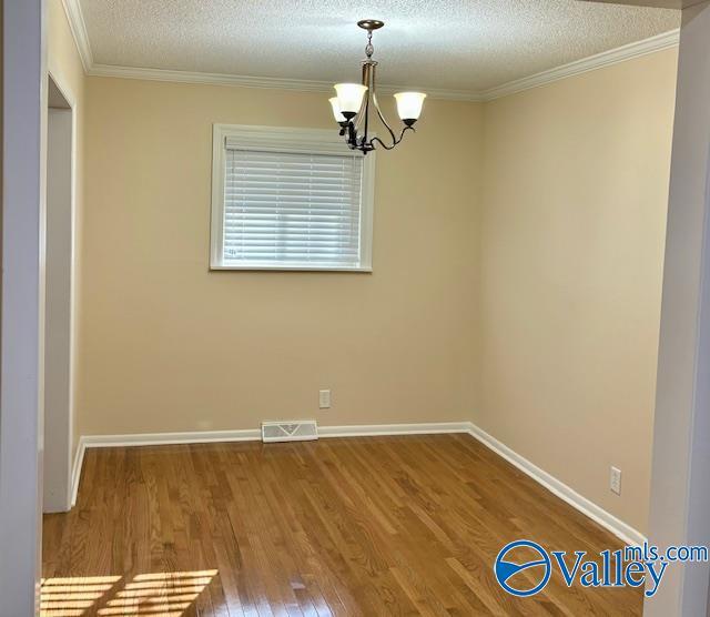 empty room featuring crown molding, a notable chandelier, visible vents, a textured ceiling, and wood finished floors