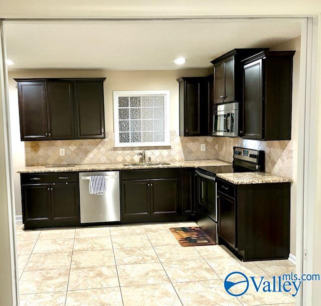 kitchen featuring appliances with stainless steel finishes, light stone countertops, a sink, and light tile patterned floors