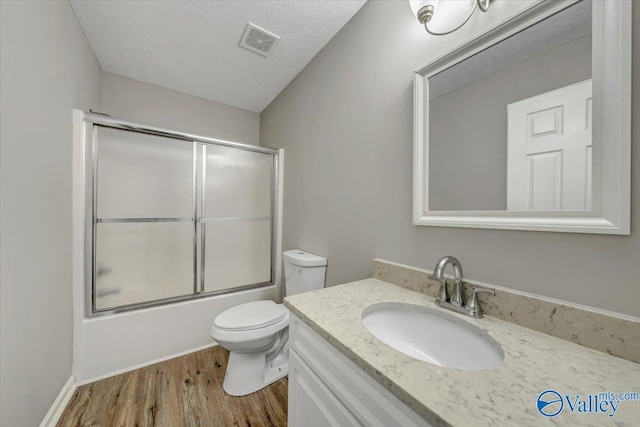 full bathroom featuring hardwood / wood-style flooring, bath / shower combo with glass door, vanity, a textured ceiling, and toilet