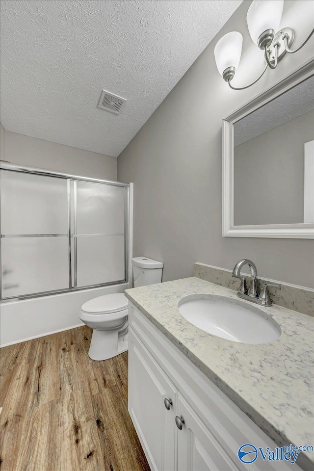 full bathroom with enclosed tub / shower combo, hardwood / wood-style floors, vanity, a textured ceiling, and toilet