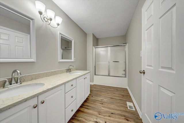 bathroom featuring hardwood / wood-style flooring, vanity, a textured ceiling, and shower / bath combination with glass door