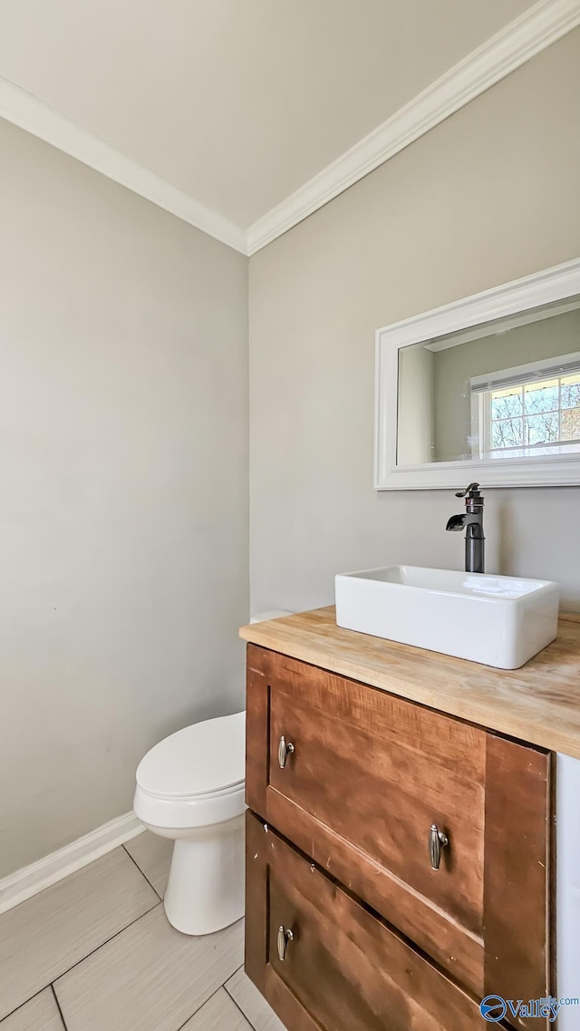 half bathroom with toilet, baseboards, crown molding, and vanity