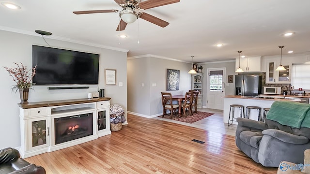 living area with light wood-type flooring, visible vents, and crown molding