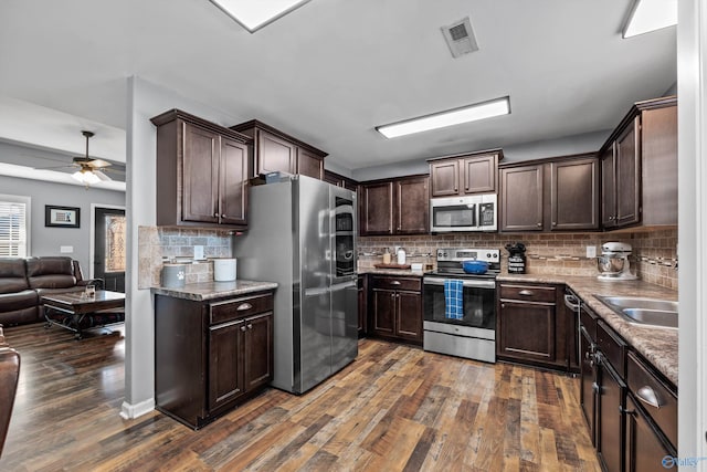 kitchen featuring a sink, stainless steel appliances, dark brown cabinetry, open floor plan, and dark wood-type flooring